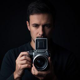 Instructor Noah Bhatti holding a medium format camera beside a dark backdrop