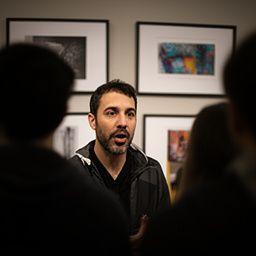 Instructor Omar Levine speaking with students beside framed portfolio prints